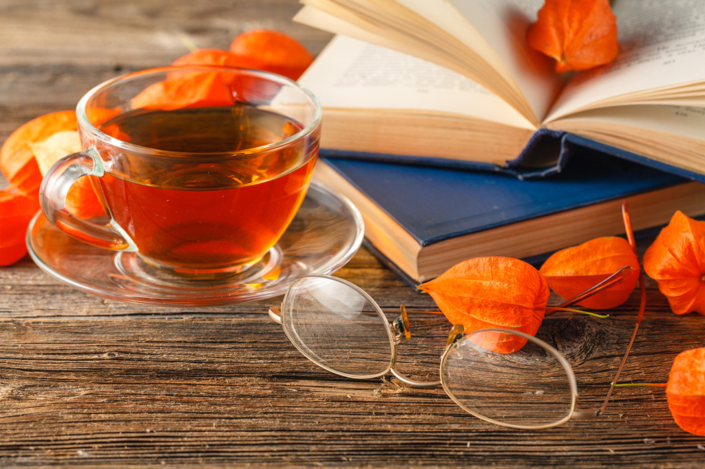 Hot coffee, vintage book, glasses and autumn leaves on wood background - relax or retirement concept